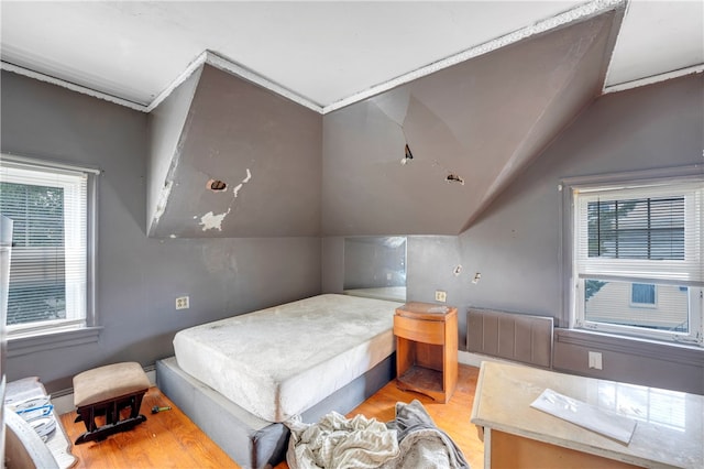 bedroom with light hardwood / wood-style flooring, vaulted ceiling, and radiator