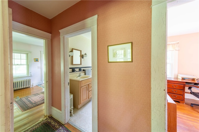 hallway with radiator heating unit, sink, and light hardwood / wood-style flooring