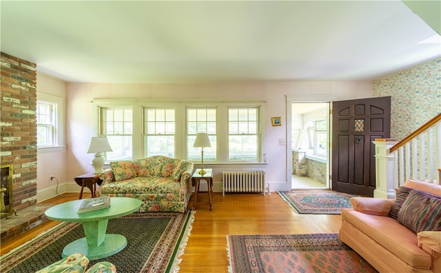 living room featuring a brick fireplace, a wealth of natural light, light wood-type flooring, and radiator heating unit