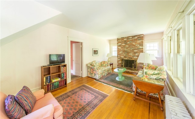 living room featuring a fireplace, brick wall, light hardwood / wood-style flooring, and radiator