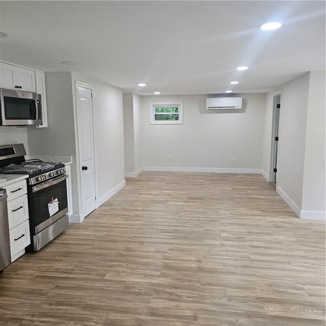 kitchen with stainless steel appliances, white cabinetry, a wall mounted air conditioner, and light hardwood / wood-style flooring