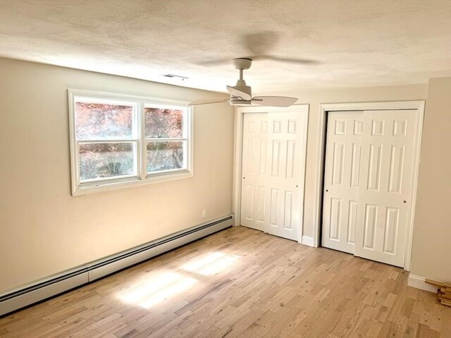 unfurnished bedroom with light hardwood / wood-style flooring, ceiling fan, baseboard heating, a textured ceiling, and multiple closets