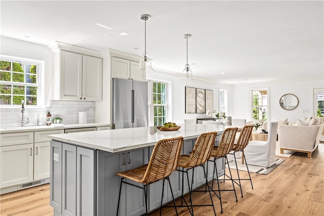 kitchen featuring light stone countertops, high end fridge, a healthy amount of sunlight, white cabinets, and a center island