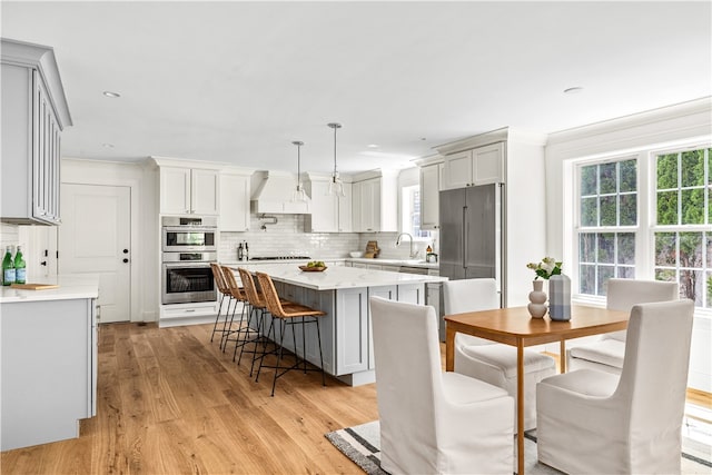 kitchen with sink, appliances with stainless steel finishes, pendant lighting, a kitchen island, and light wood-type flooring