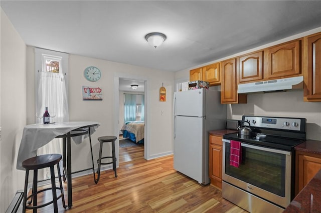 kitchen with stainless steel range with electric stovetop, light wood-type flooring, white refrigerator, a baseboard radiator, and a kitchen breakfast bar