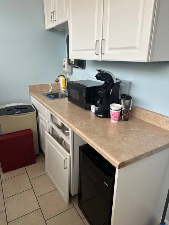 kitchen featuring black microwave, wine cooler, a sink, and white cabinets