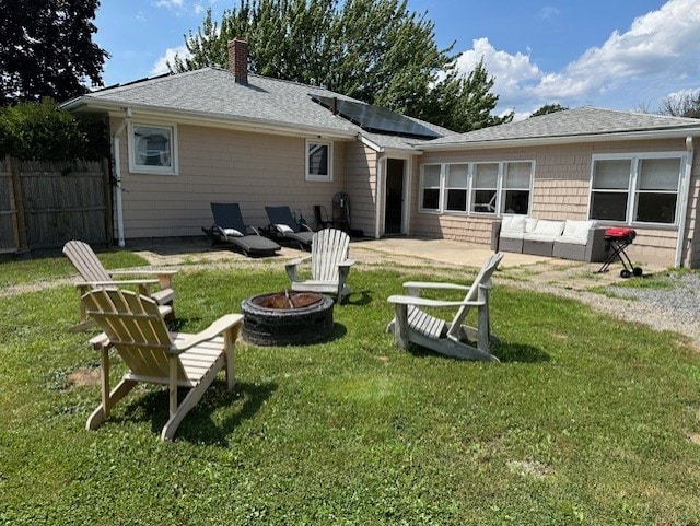 rear view of property featuring a yard, a chimney, solar panels, an outdoor fire pit, and fence