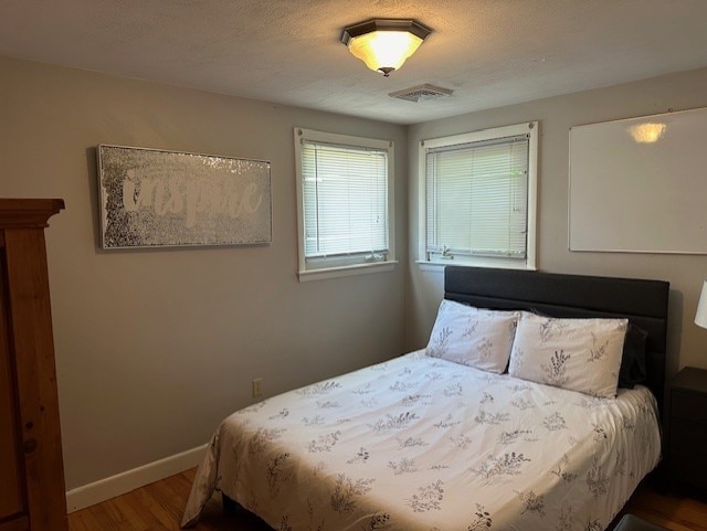 bedroom featuring baseboards, a textured ceiling, visible vents, and wood finished floors