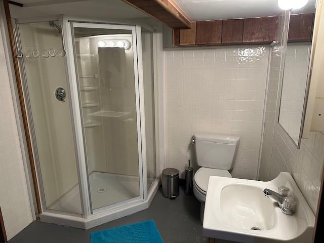 bathroom featuring sink, toilet, an enclosed shower, and tile walls