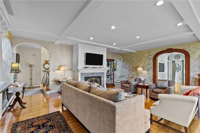 living room featuring beamed ceiling, a large fireplace, light hardwood / wood-style flooring, and a baseboard radiator