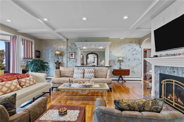 living room featuring beamed ceiling, light hardwood / wood-style flooring, a premium fireplace, and a baseboard radiator