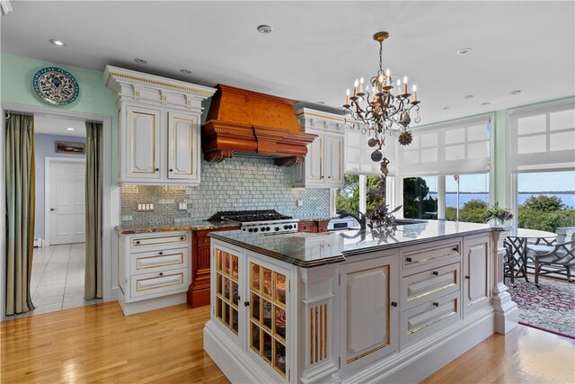 kitchen with a kitchen island with sink, light hardwood / wood-style flooring, backsplash, decorative light fixtures, and premium range hood