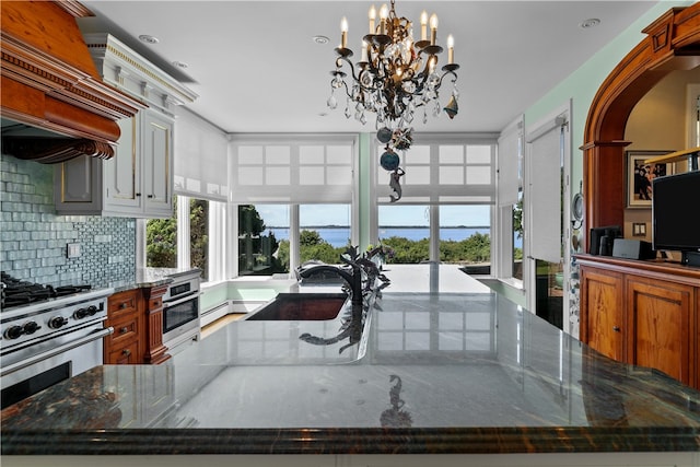 kitchen with backsplash, stainless steel appliances, custom exhaust hood, dark stone counters, and sink