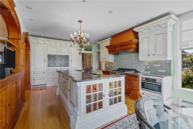 kitchen featuring tasteful backsplash, a kitchen island, stainless steel appliances, light wood-type flooring, and decorative light fixtures