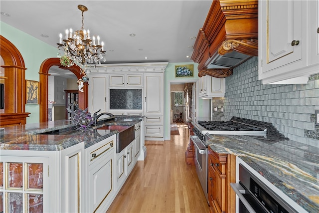 kitchen with stainless steel stove, sink, tasteful backsplash, and white cabinetry