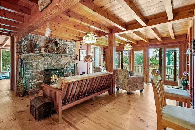 living room with a stone fireplace, light hardwood / wood-style flooring, beam ceiling, and wooden ceiling