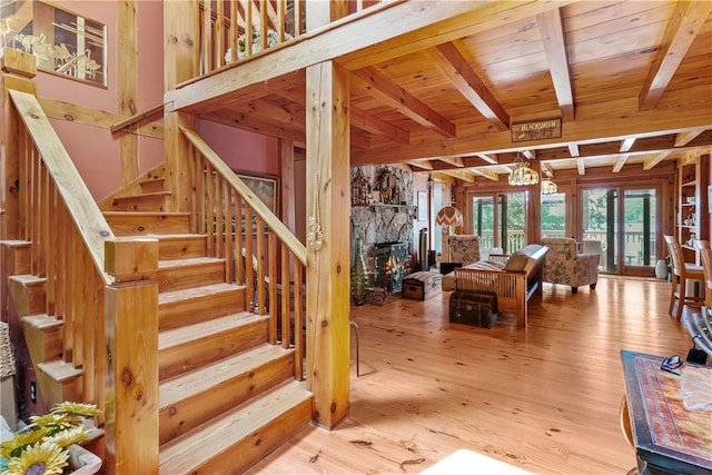 stairs with beam ceiling, a stone fireplace, wood-type flooring, and wooden ceiling