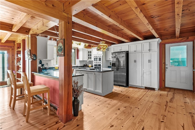 kitchen featuring appliances with stainless steel finishes, white cabinets, beamed ceiling, and light hardwood / wood-style floors