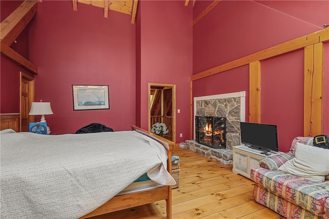 bedroom with beam ceiling, hardwood / wood-style floors, a fireplace, and high vaulted ceiling