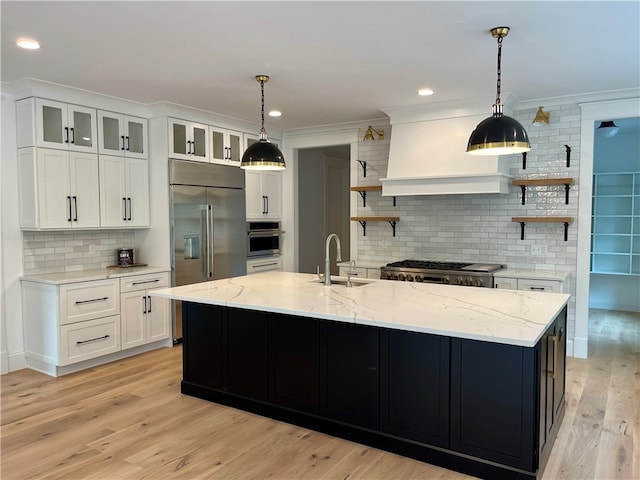 kitchen with custom range hood, tasteful backsplash, light wood-type flooring, an island with sink, and sink