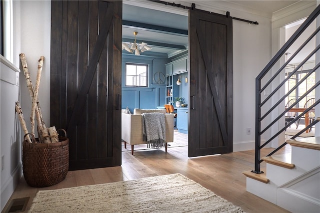 entryway featuring crown molding, an inviting chandelier, a barn door, beam ceiling, and light hardwood / wood-style flooring