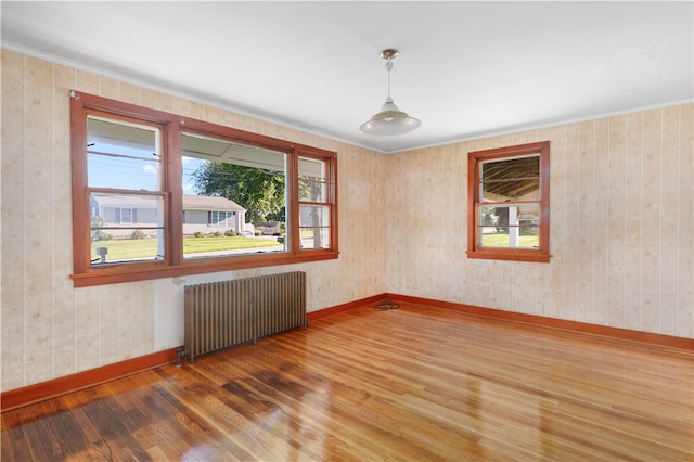 unfurnished room featuring wood walls, hardwood / wood-style flooring, and radiator heating unit