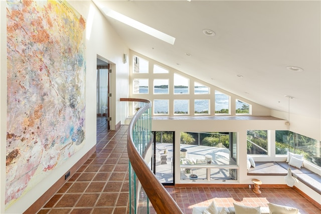 hall featuring high vaulted ceiling, dark tile patterned flooring, and a skylight