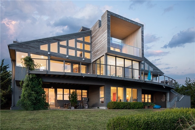 back house at dusk featuring a balcony and a lawn