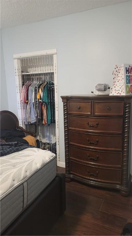 bedroom with a textured ceiling, dark wood-type flooring, and a closet