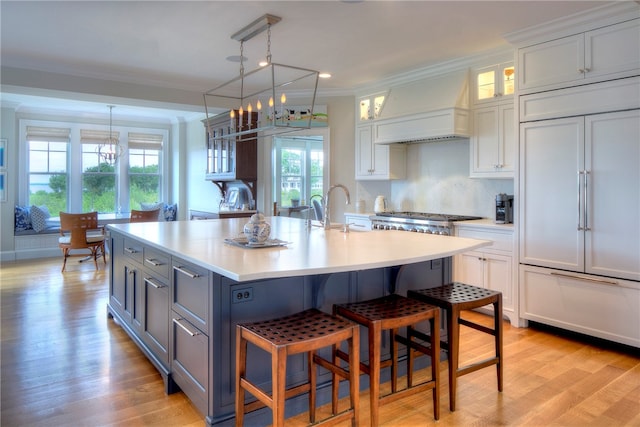 kitchen featuring premium range hood, light hardwood / wood-style floors, pendant lighting, and paneled refrigerator