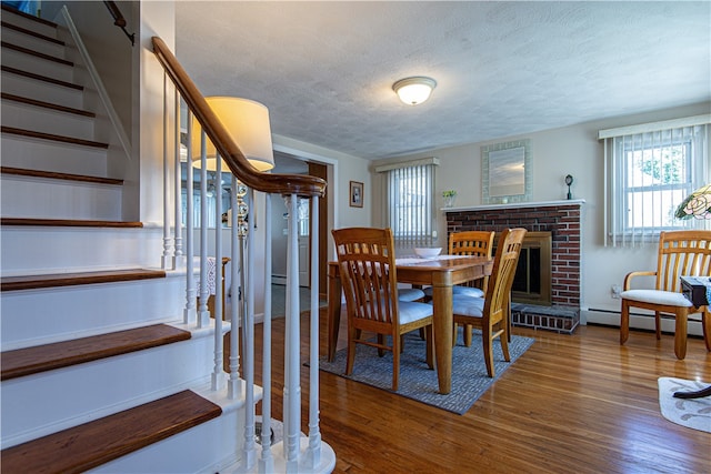 dining room with a brick fireplace, a textured ceiling, a baseboard radiator, and dark hardwood / wood-style flooring