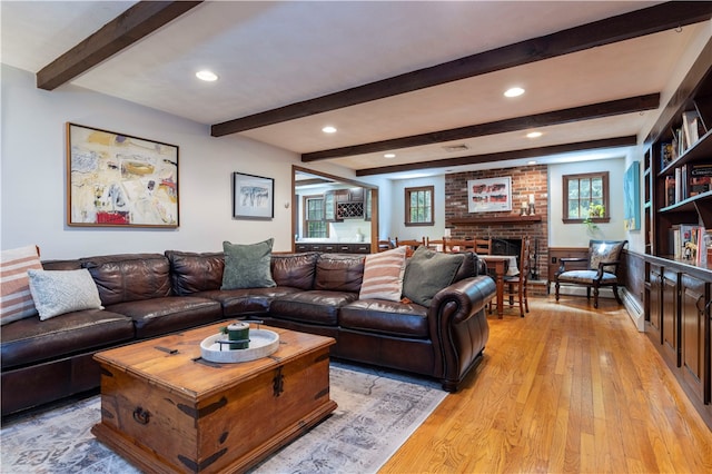 living room featuring light wood-type flooring, a brick fireplace, beamed ceiling, and brick wall