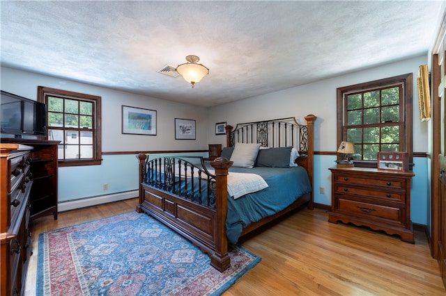 bedroom featuring multiple windows, baseboard heating, and light hardwood / wood-style floors