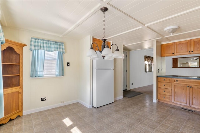 kitchen featuring visible vents, brown cabinetry, dark countertops, freestanding refrigerator, and an inviting chandelier