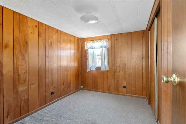 empty room featuring carpet flooring, wooden walls, and baseboards