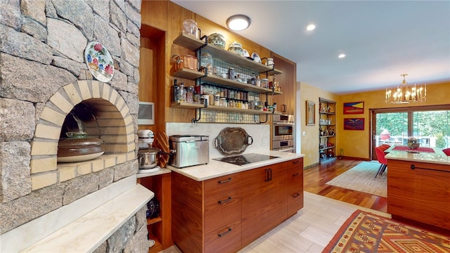 kitchen with an inviting chandelier, black electric stovetop, double oven, light hardwood / wood-style flooring, and hanging light fixtures