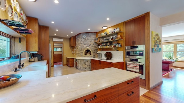 kitchen featuring sink, a stone fireplace, stainless steel double oven, light stone countertops, and light hardwood / wood-style floors