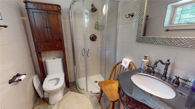 bathroom with tile walls, a shower with shower door, vanity, and toilet