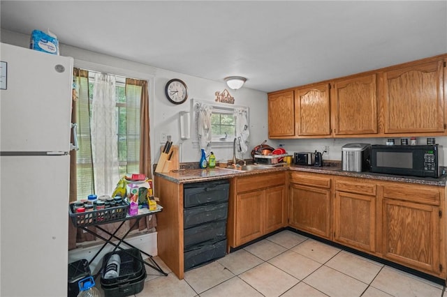 kitchen featuring black microwave, a sink, freestanding refrigerator, brown cabinets, and dark countertops