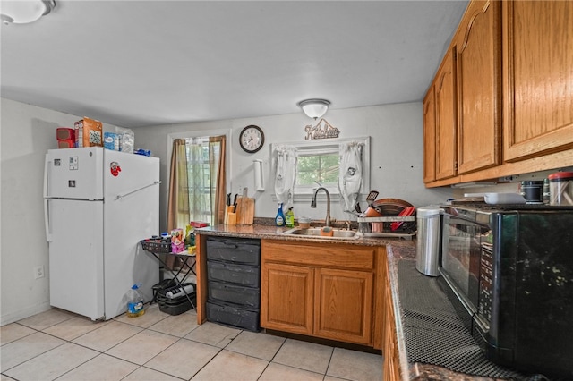 kitchen featuring sink, dark stone countertops, white refrigerator, and light tile patterned floors