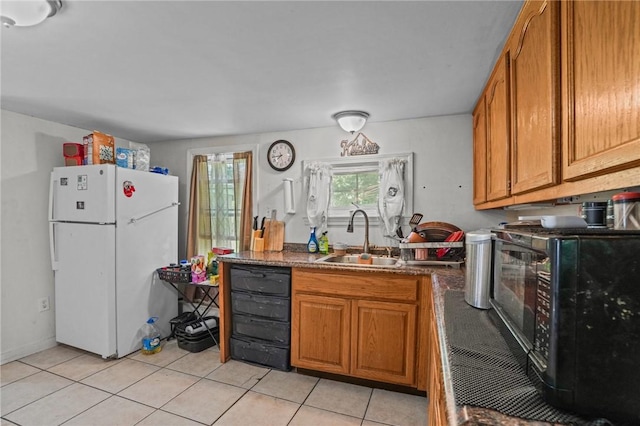 kitchen with black microwave, a sink, freestanding refrigerator, brown cabinetry, and dark countertops