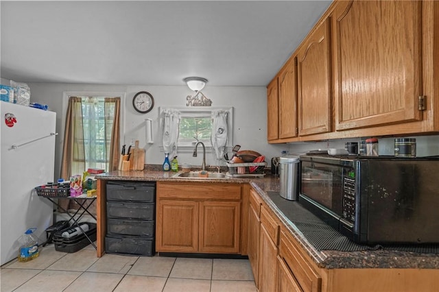 kitchen featuring light tile patterned floors, brown cabinetry, freestanding refrigerator, a sink, and black microwave