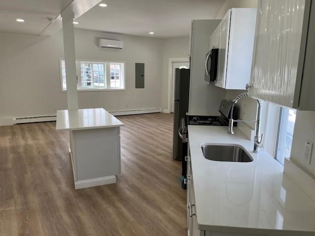 kitchen with light hardwood / wood-style flooring, a baseboard radiator, white cabinets, and electric panel