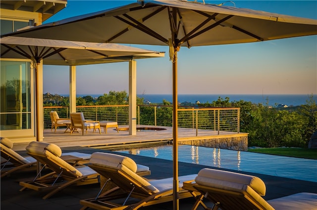 pool at dusk featuring a deck with water view