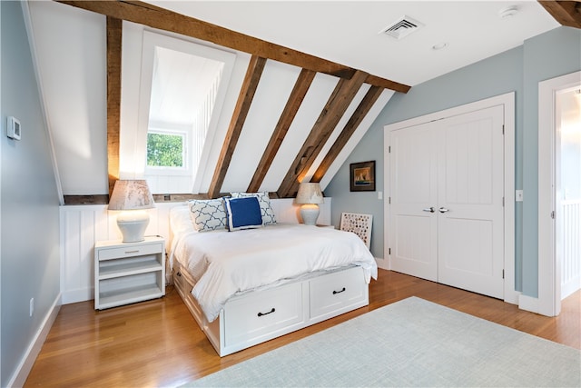 bedroom with a closet, light hardwood / wood-style floors, and vaulted ceiling with beams