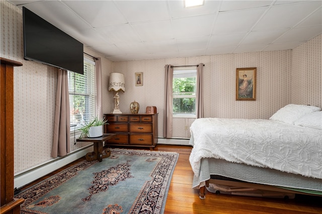 bedroom featuring baseboard heating, hardwood / wood-style floors, and multiple windows