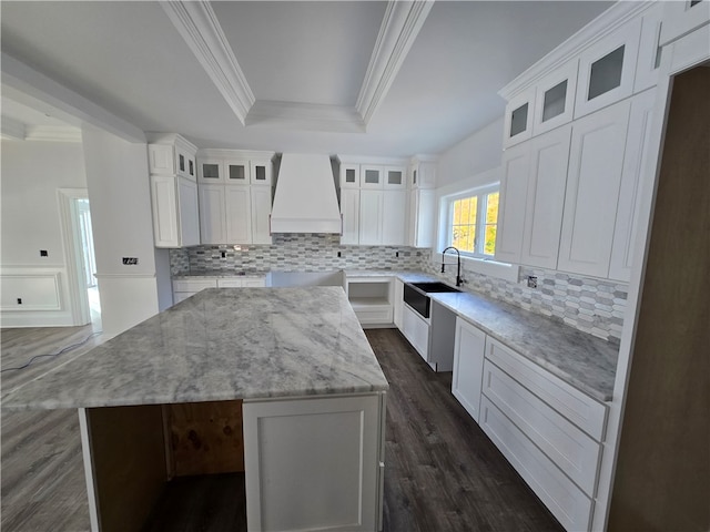 kitchen with a kitchen island, white cabinetry, custom range hood, light stone counters, and dark wood-type flooring