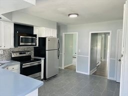 kitchen with appliances with stainless steel finishes, tile patterned floors, white cabinetry, and decorative backsplash