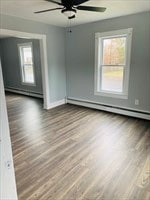 unfurnished room with a baseboard heating unit, plenty of natural light, wood-type flooring, and ceiling fan