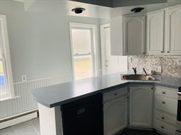 kitchen featuring light tile patterned floors, baseboard heating, sink, black dishwasher, and kitchen peninsula